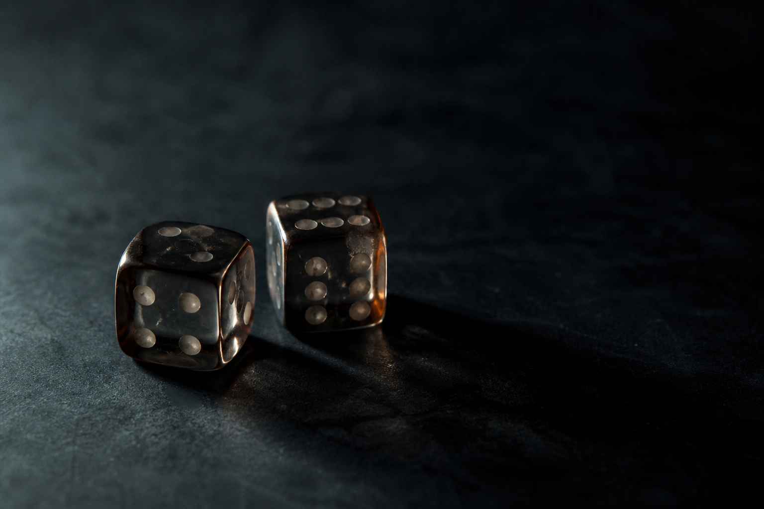 Dice on a dark surface under moody side lighting